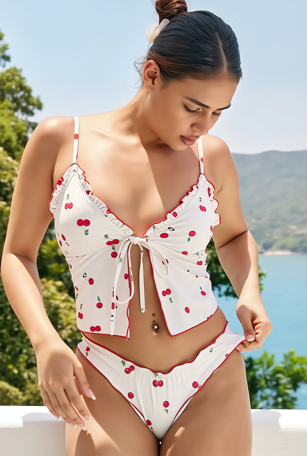 White cherry print bikini with ruffled trim and tie-front top, worn by woman overlooking coastal landscape