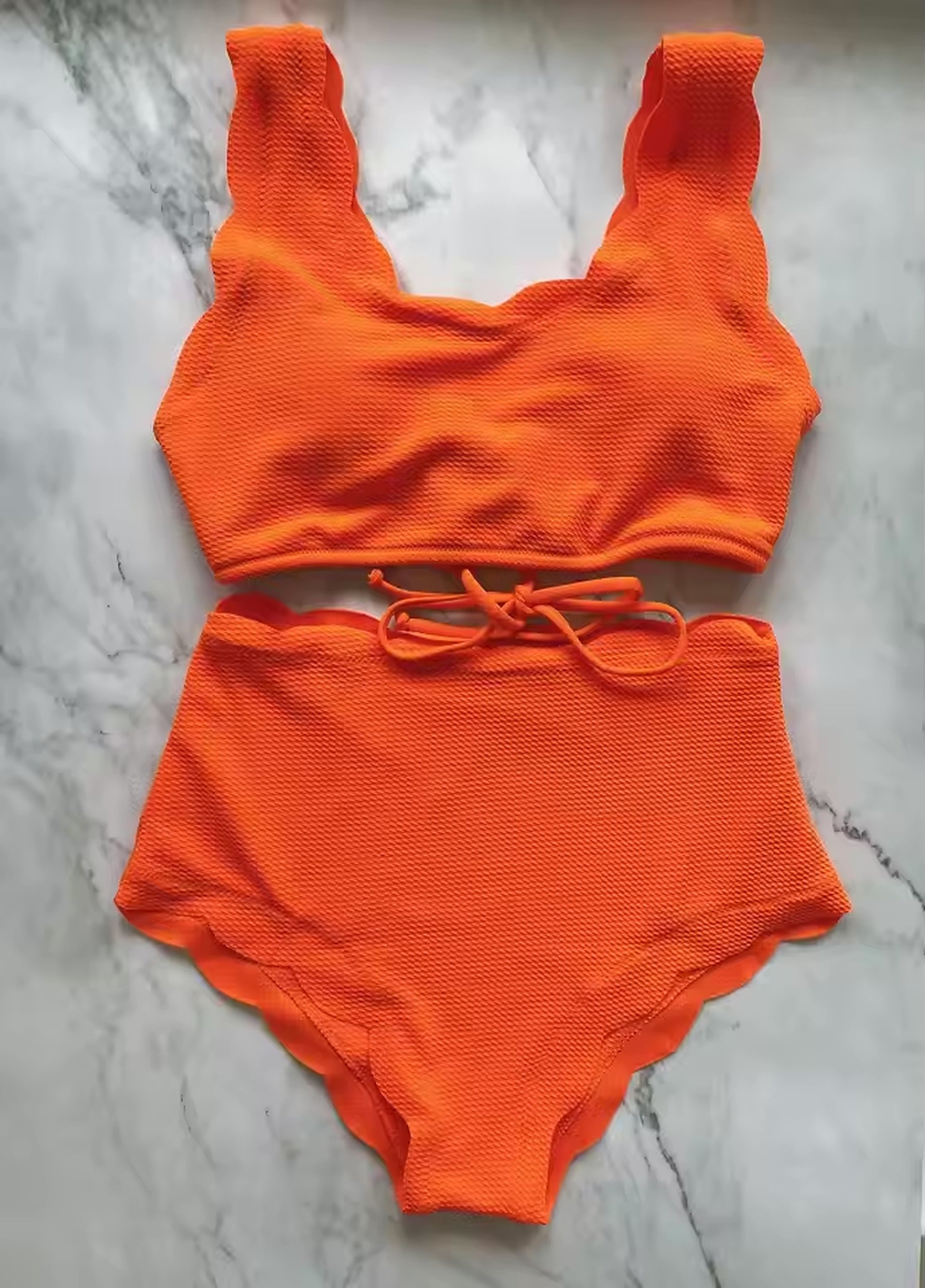 Bright orange textured bikini with padded crop top and high-waisted bottoms with drawstring tie on marble background