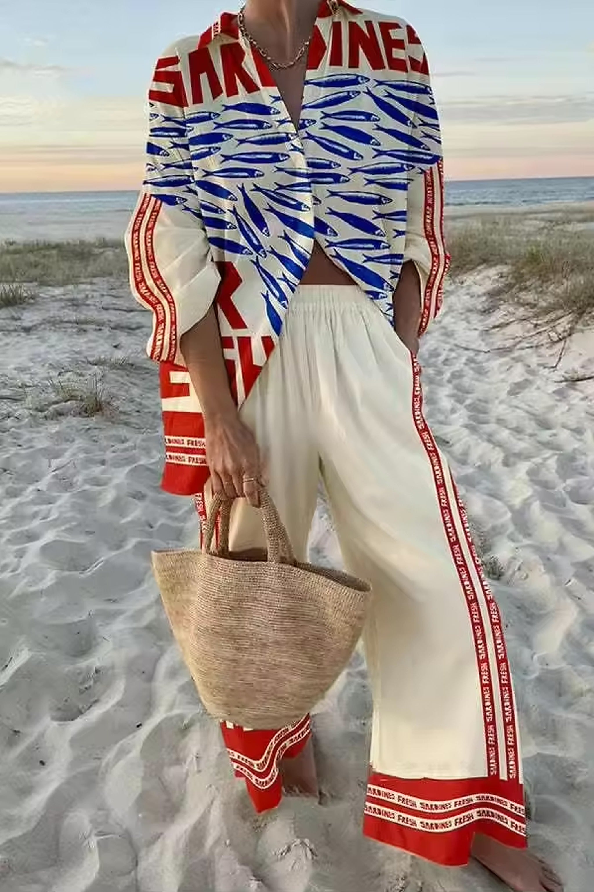 Woman wearing red, white and blue fish-print bikini on beach with matching sarong and straw bag