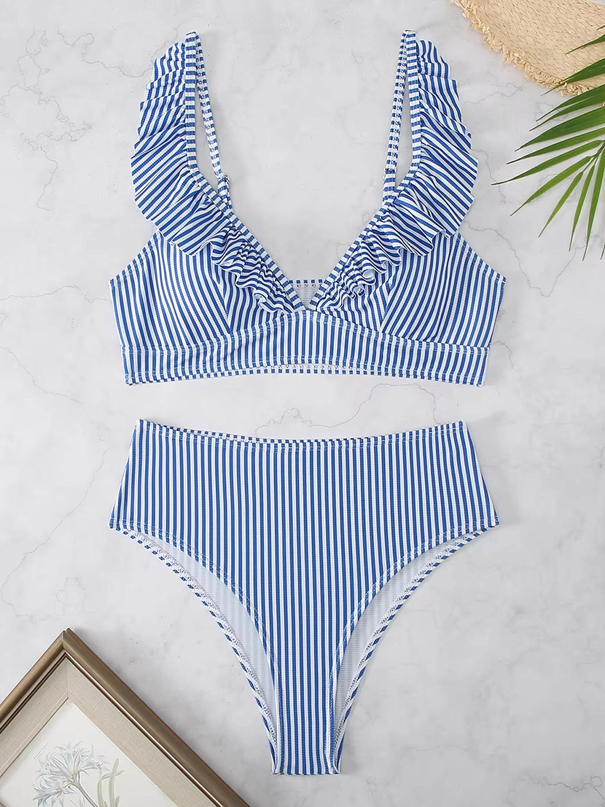 Blue and white striped bikini with ruffled neckline and high-waisted bottoms, styled flat lay on marble surface.