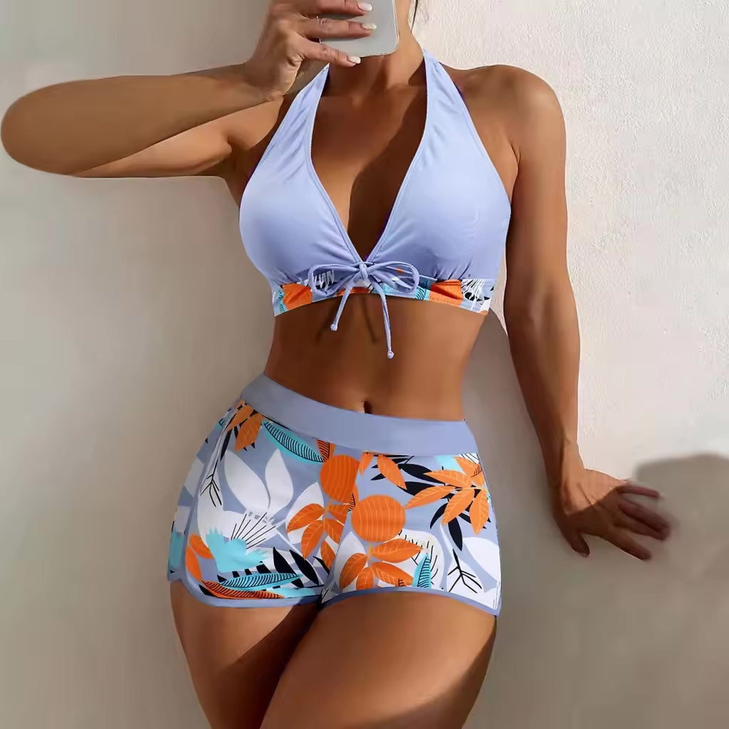 Woman wearing light blue halter bikini top with orange floral print tie-front detail and matching patterned shorts.