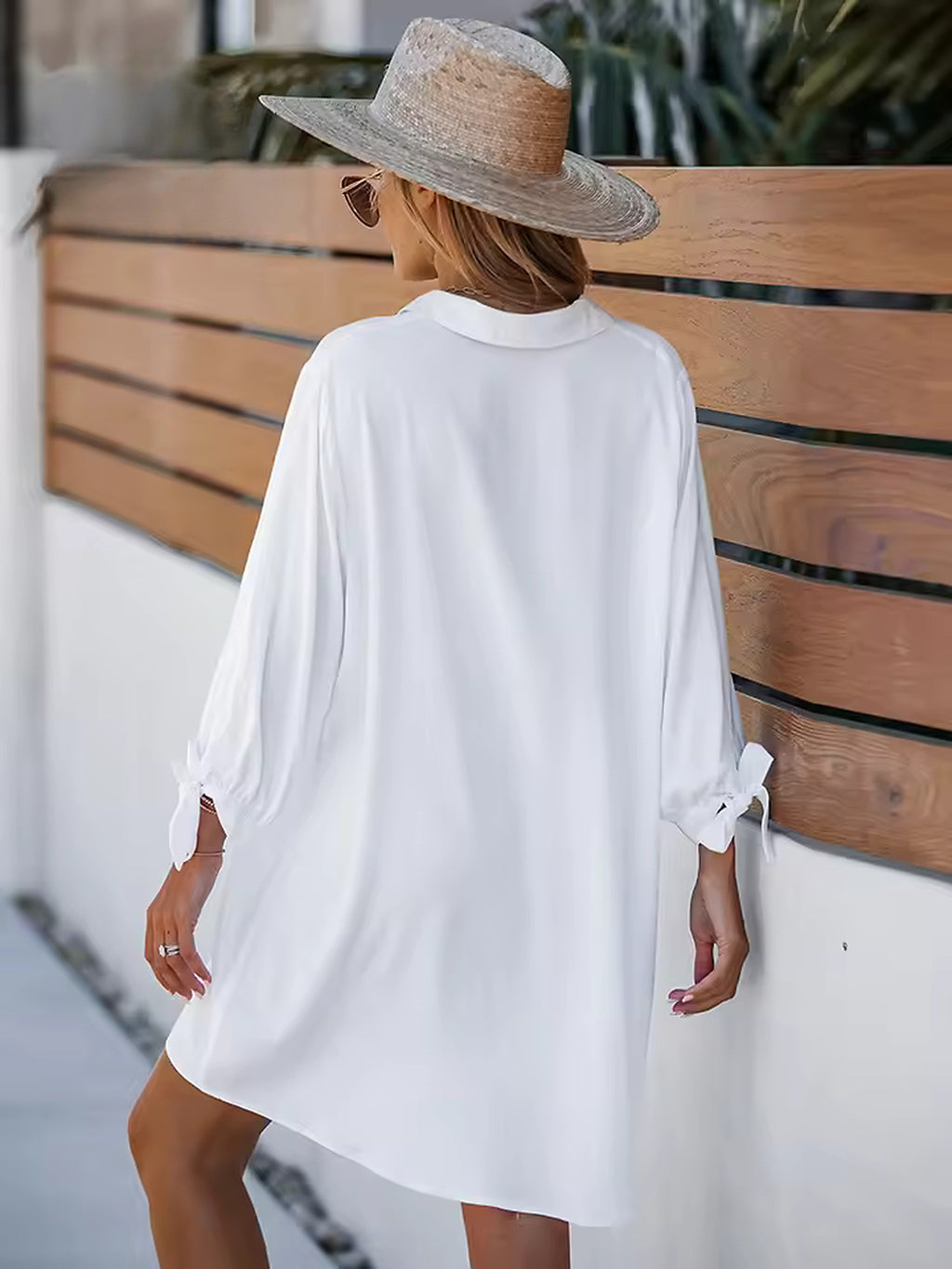 White oversized beach shirt with rolled sleeves worn over bikini, styled with straw hat by wooden fence.