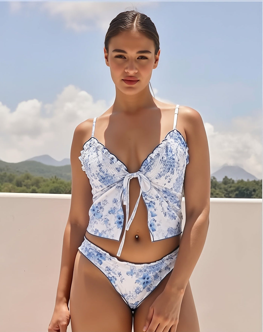 Woman wearing blue floral print bikini with ruffled bow-front top and matching bottoms against scenic mountain landscape