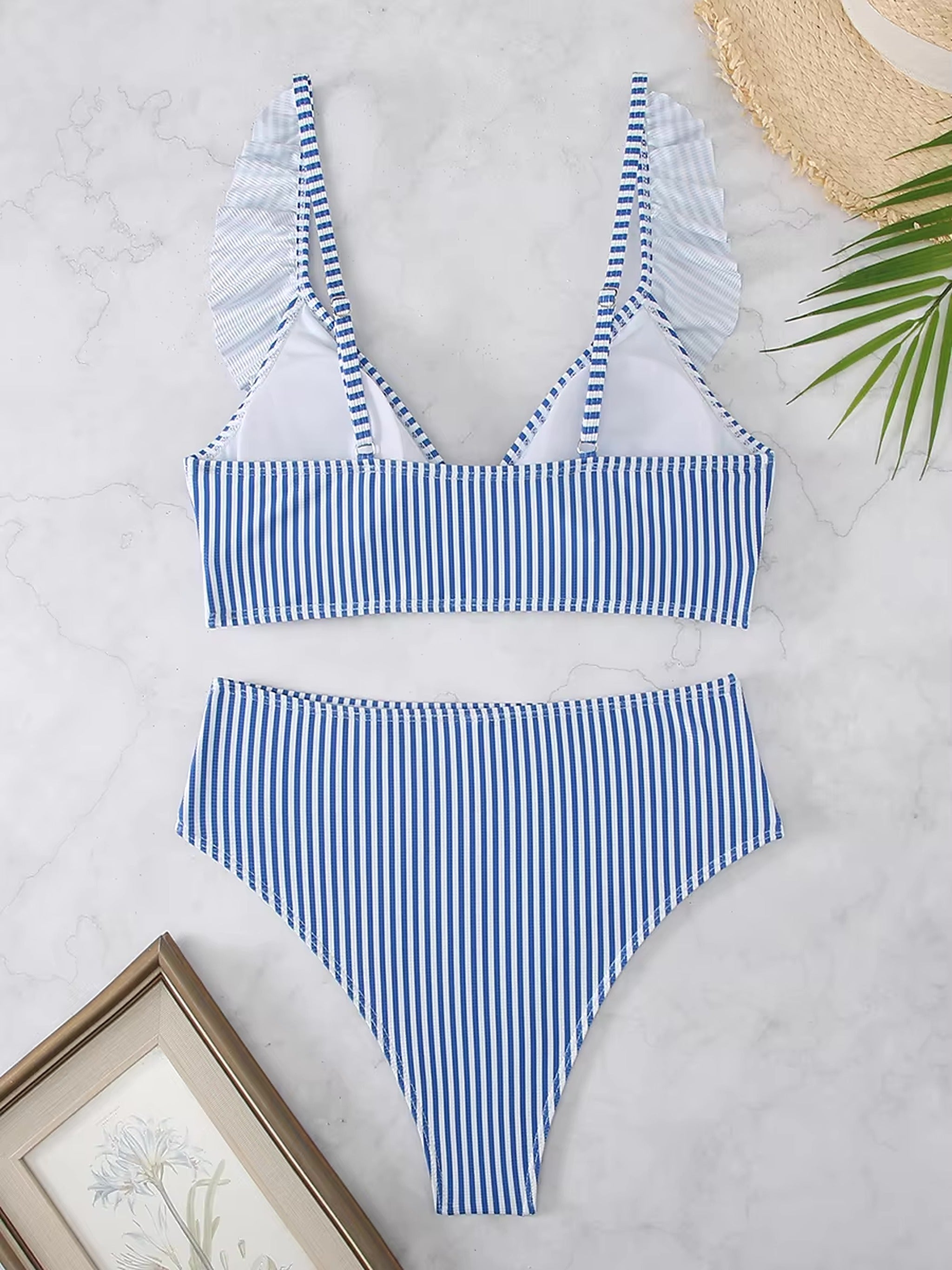 Blue and white striped bikini with ruffled shoulder details and high-waisted bottoms on marble background