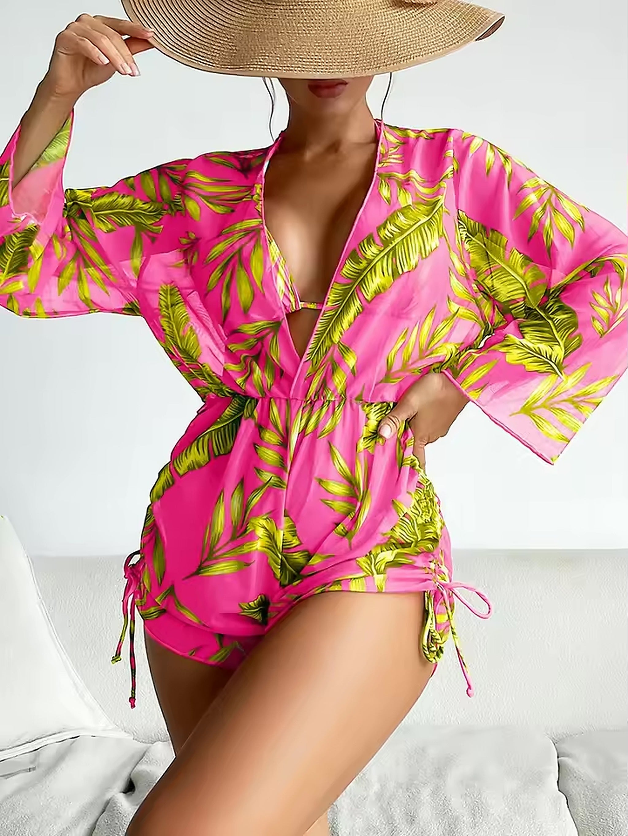 Woman wearing hot pink tropical print bikini with side tie detail and matching cover-up shirt, paired with straw hat.