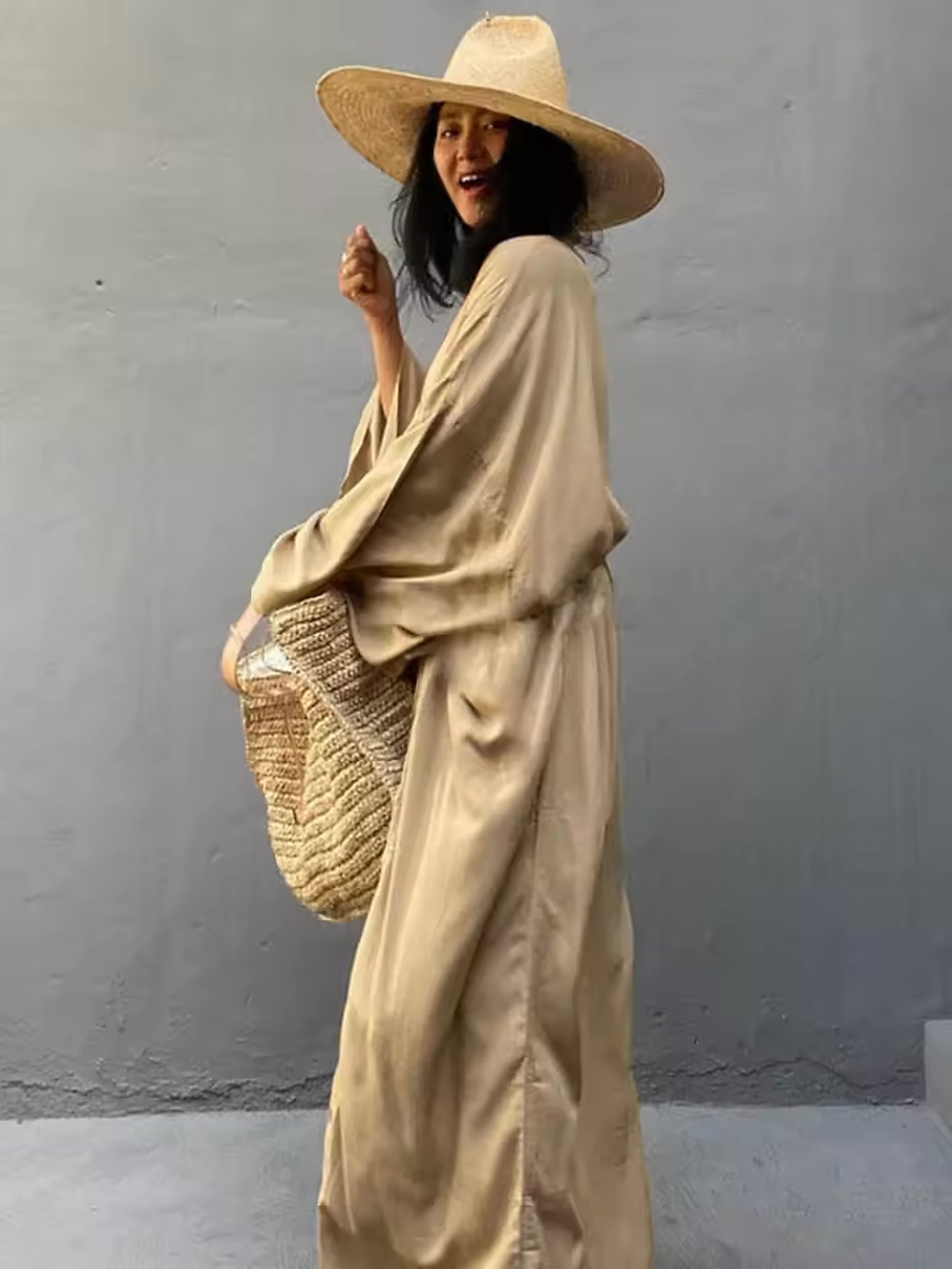 Woman wearing cream linen cover-up over swimwear with straw hat and woven beach bag