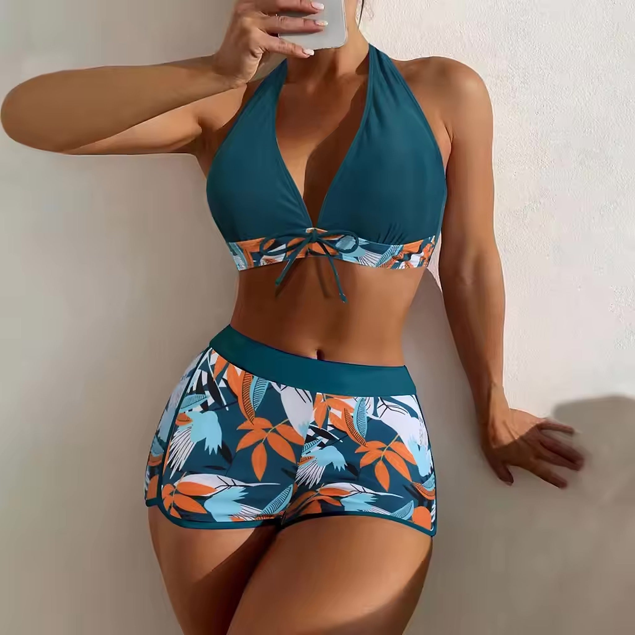 Teal halter bikini top with tropical print band and matching patterned shorts featuring orange and blue botanical design.
