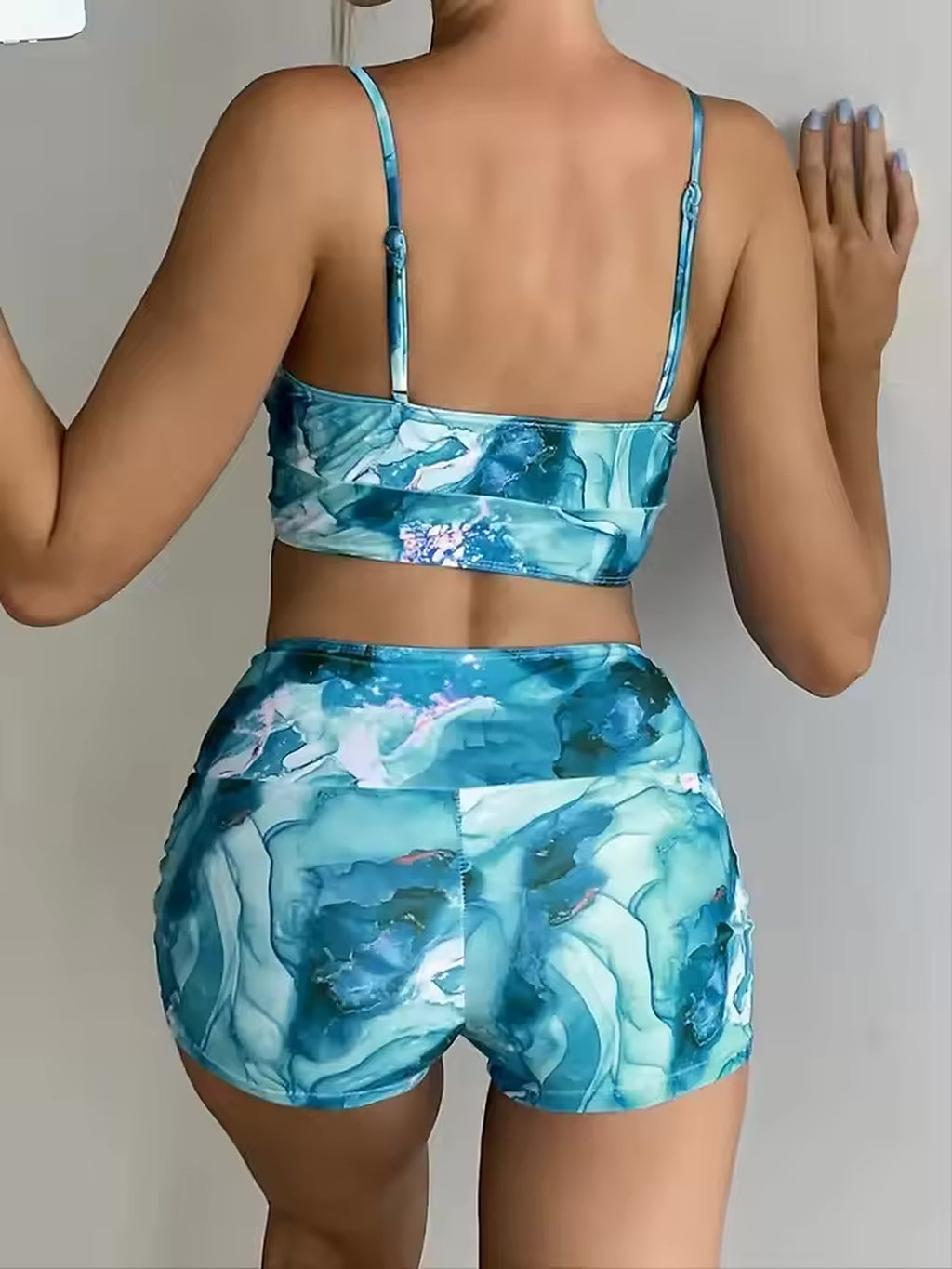 Woman wearing blue watercolor print bikini set with thin straps, shown from back view against white background.
