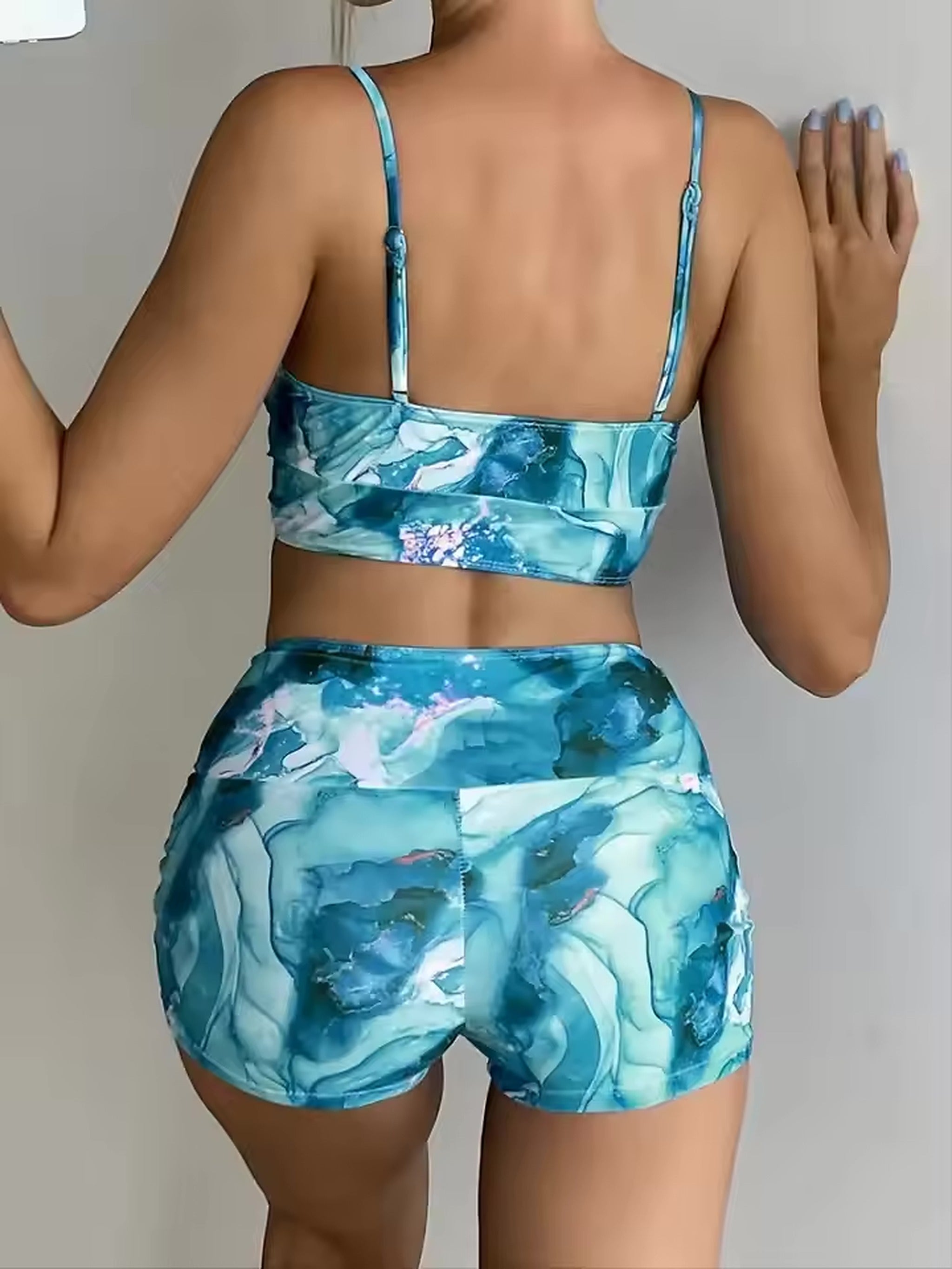 Woman wearing blue watercolor print bikini set with thin straps, shown from back view against white background.