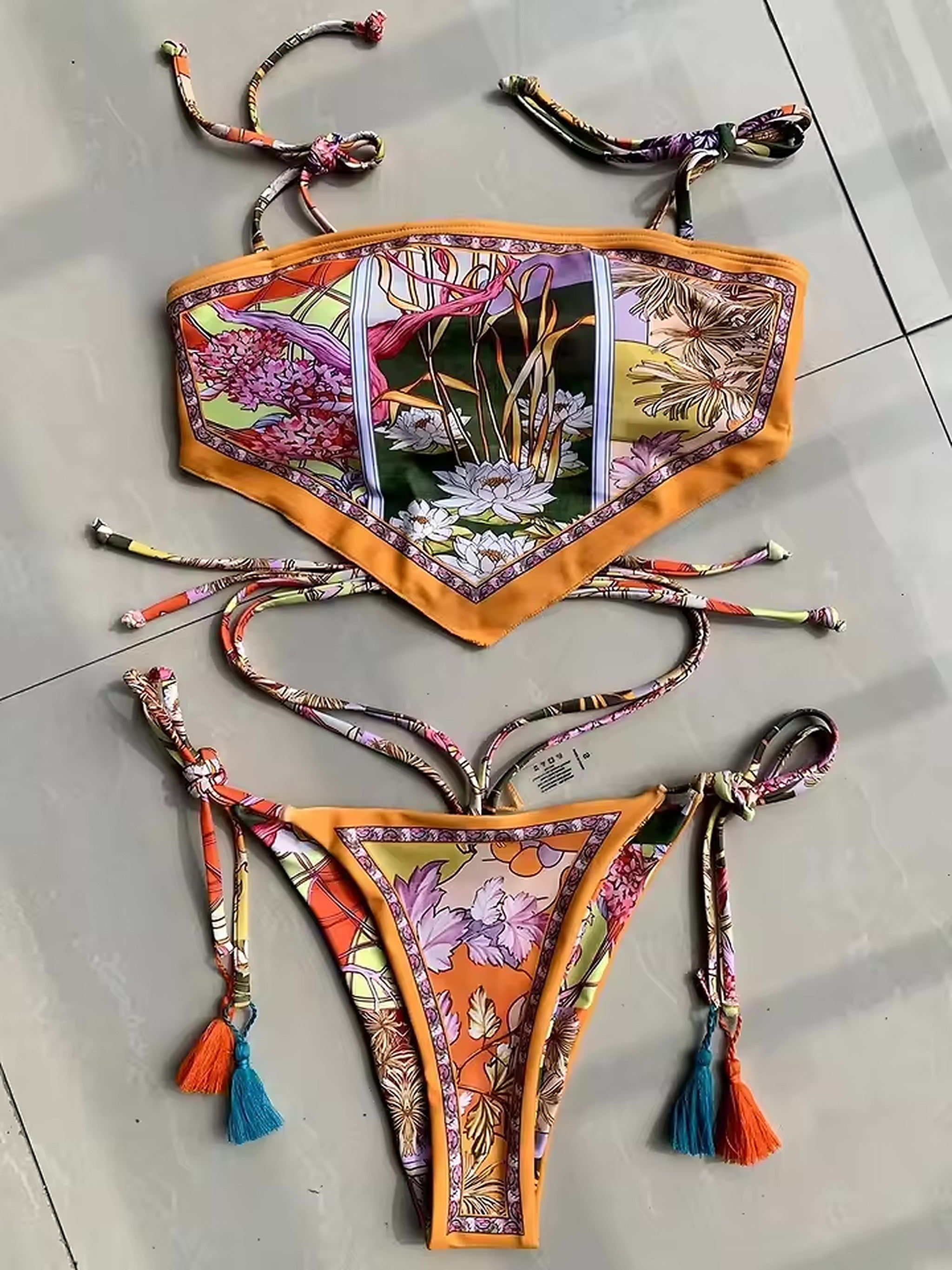 Zanzibar Heat bikini with vibrant floral print, orange trim, patterned tie straps, and colorful tassels displayed flat lay.