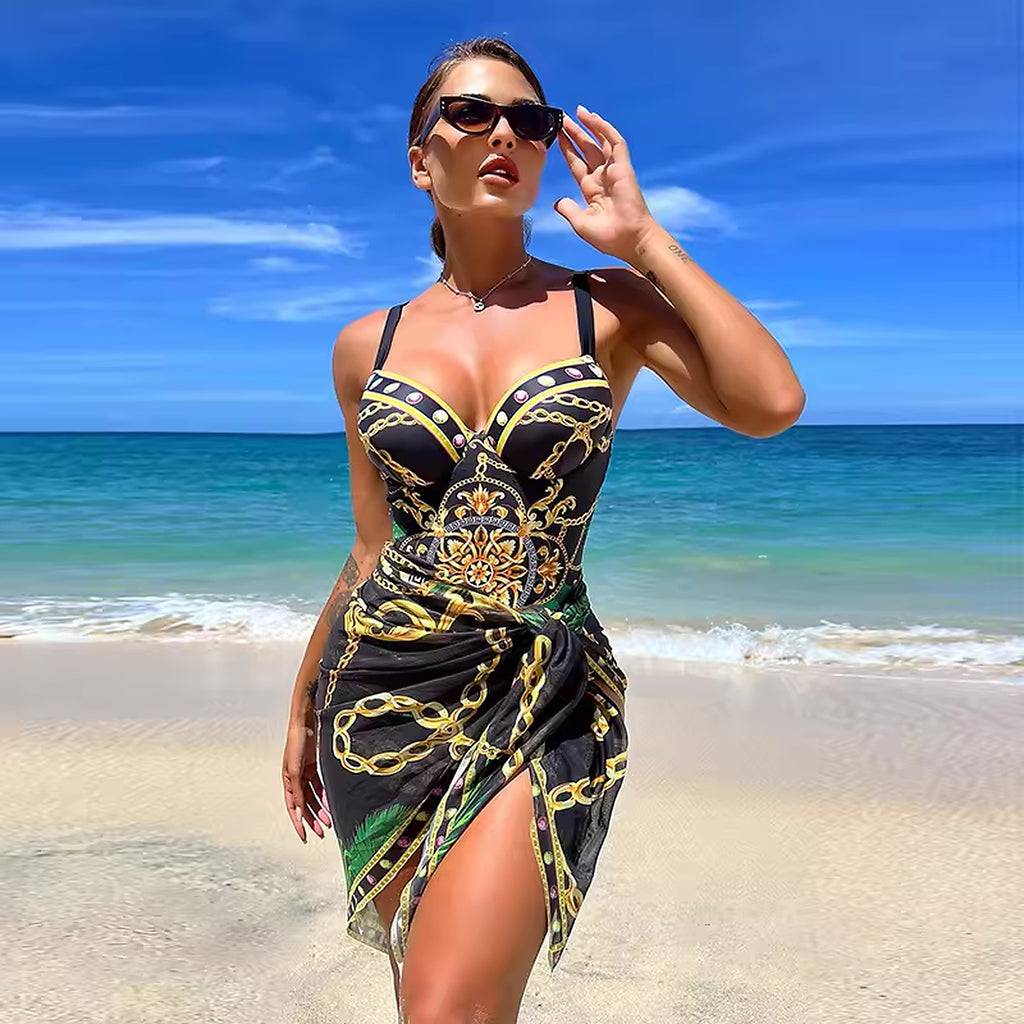 Woman wearing black and gold chain-print bikini with matching sarong on beach with turquoise ocean and blue sky.