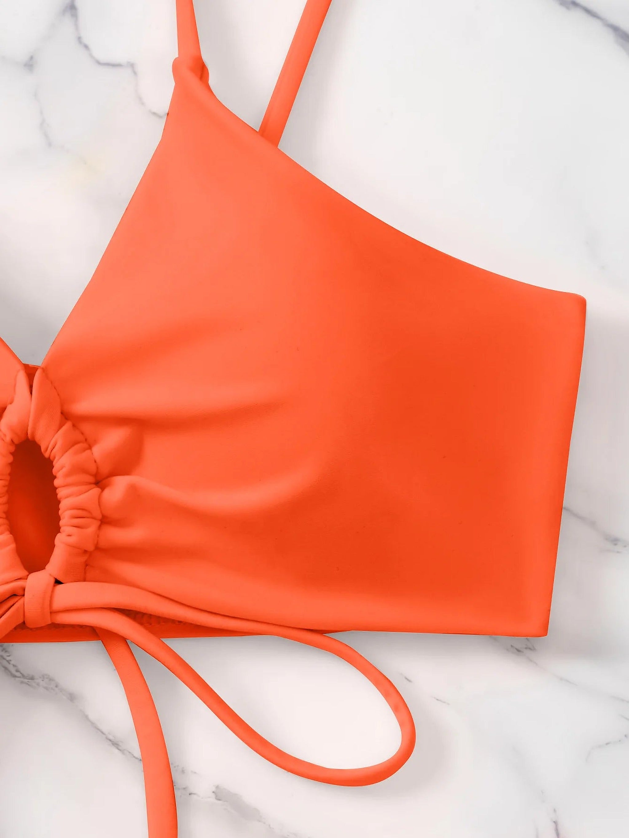 Bright coral bikini top with adjustable straps and ruched side details on marble background