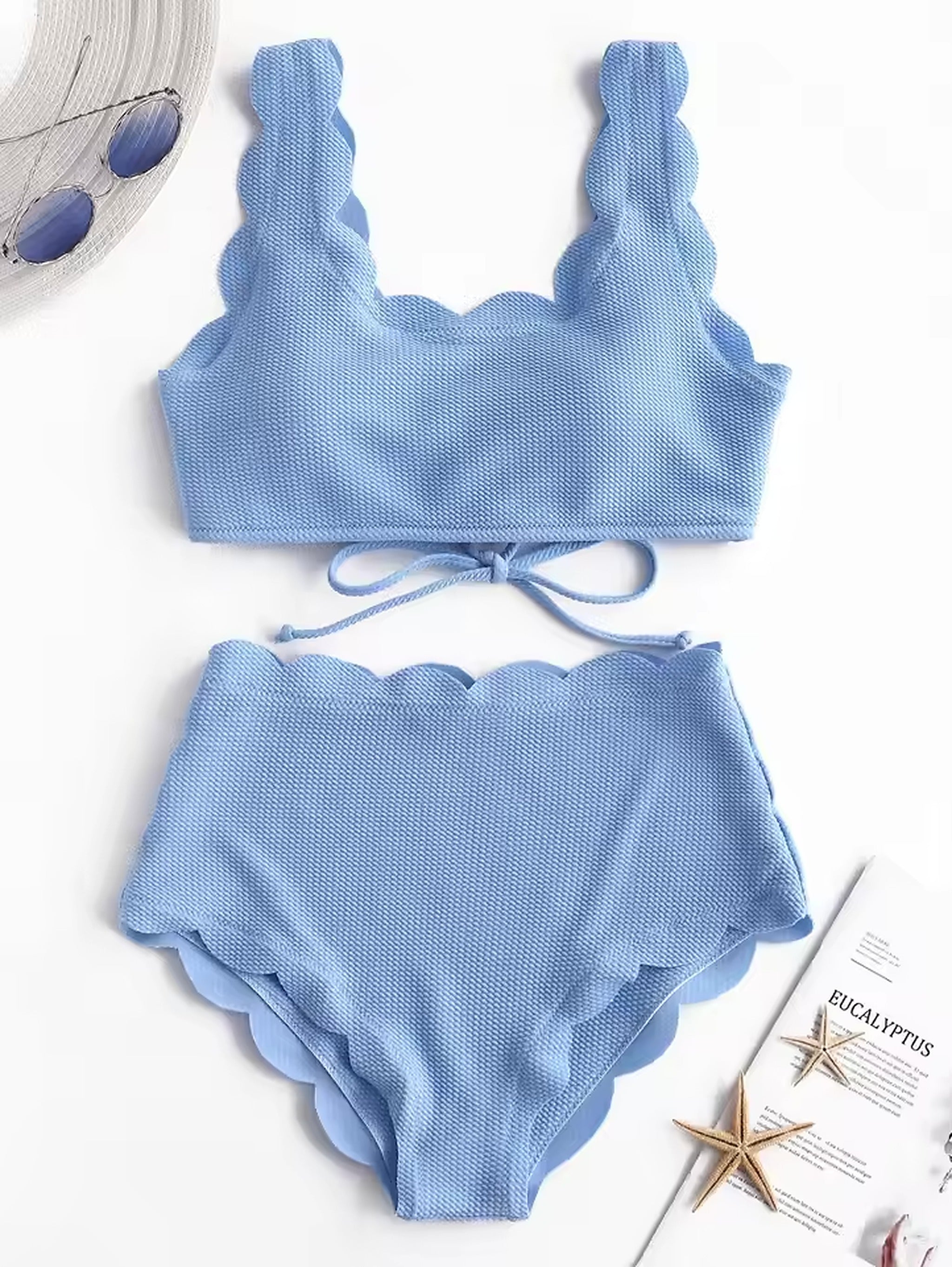 Light blue textured bikini with scalloped edges and tie-front design, paired with sunglasses and beach accessories.