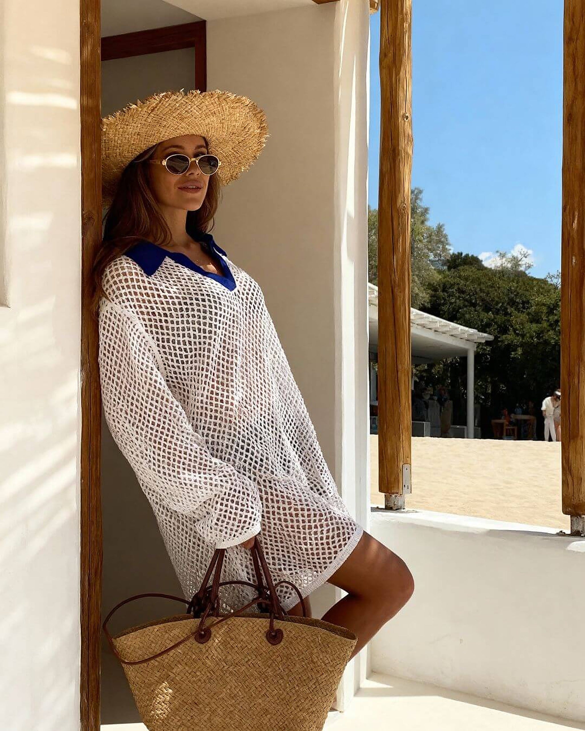 Woman wearing white mesh swimsuit cover-up over navy bikini at beach house doorway
