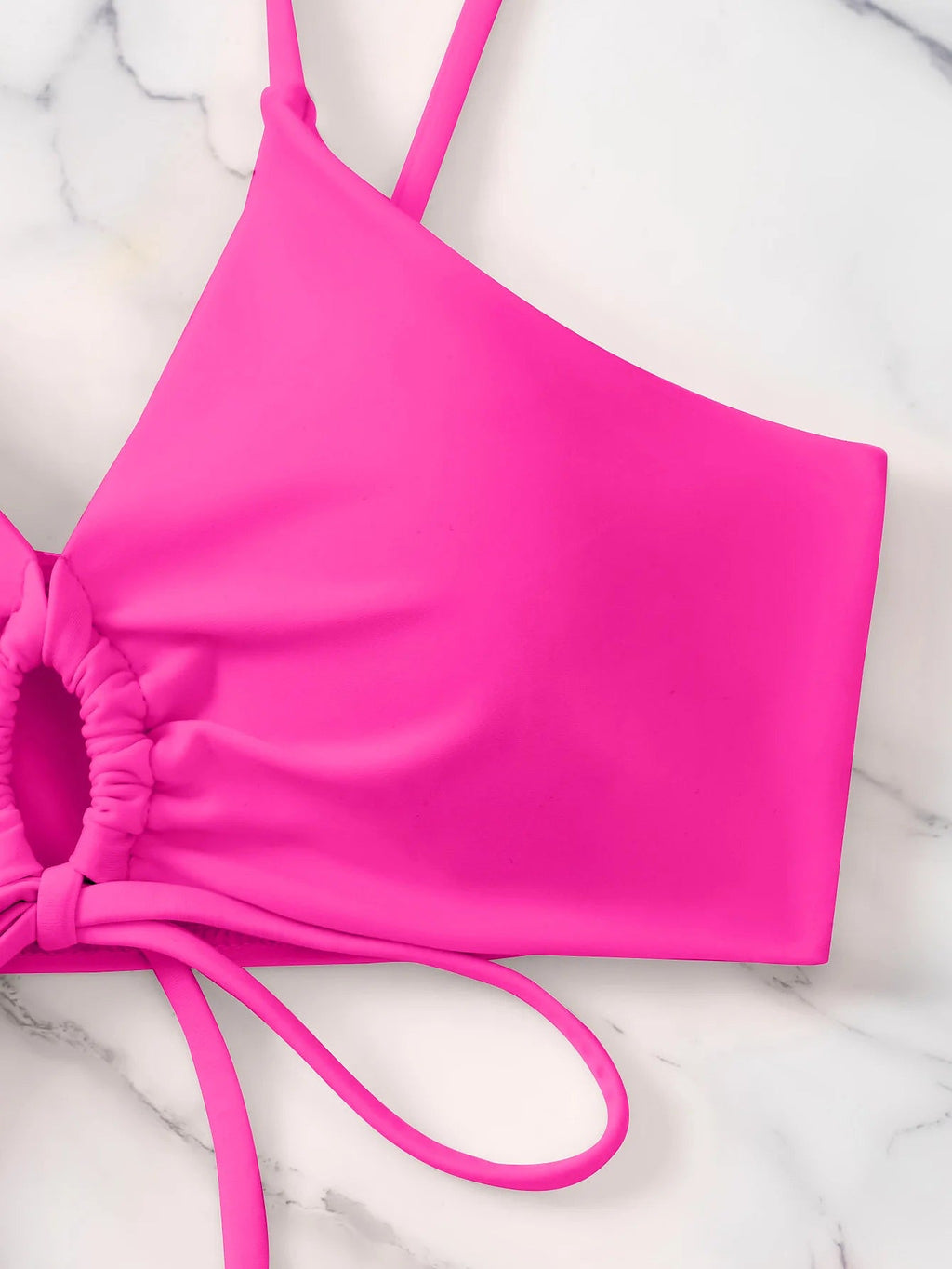 Bright pink bikini top with ruched side detailing and adjustable straps on marble background