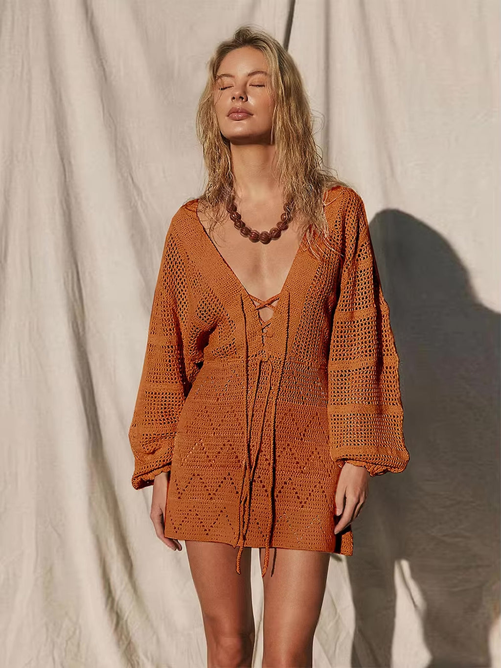 Woman wearing burnt orange crochet bikini cover-up dress with lace-up front detail and long sleeves
