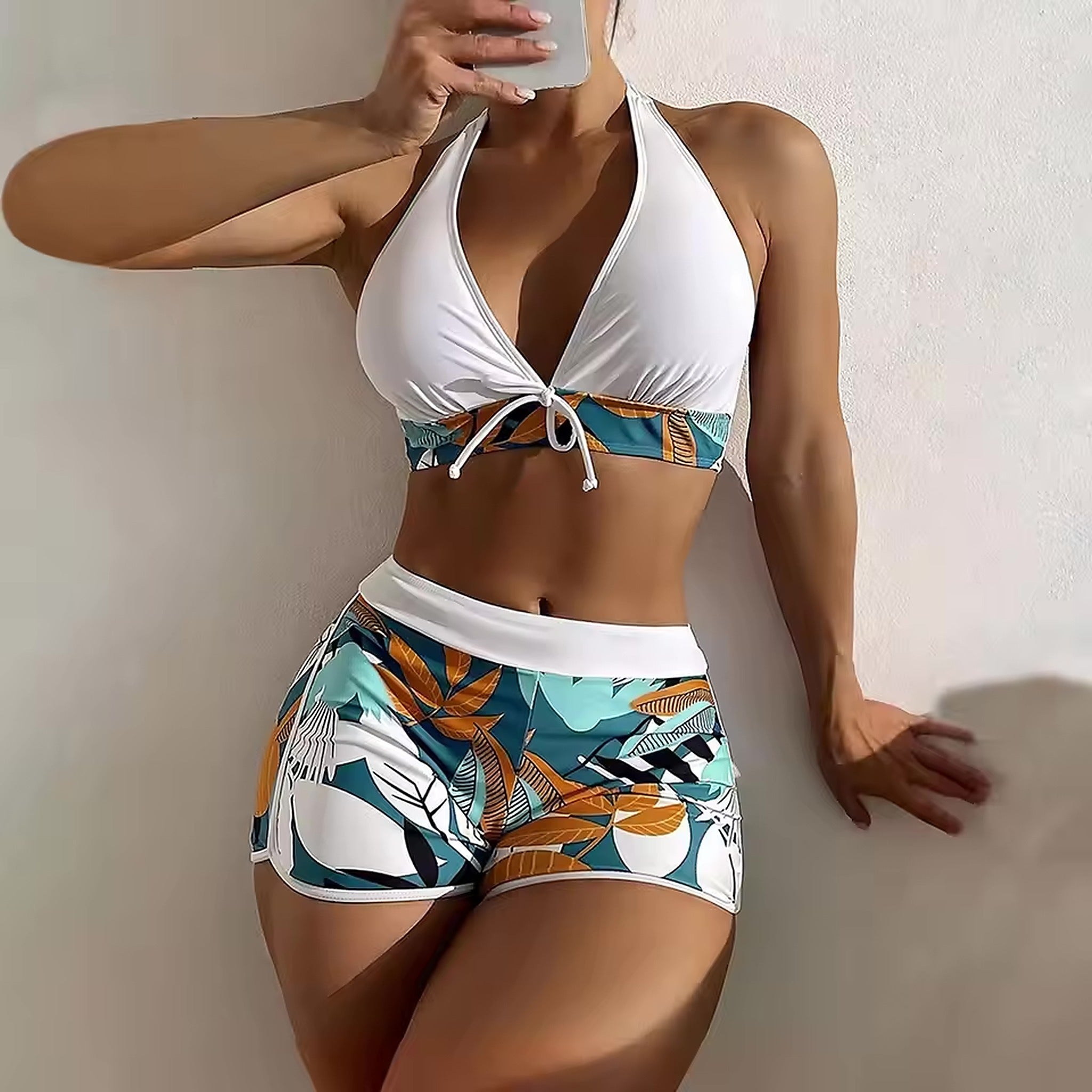 White halter bikini top with tropical leaf-print high-waisted shorts featuring teal, orange, and white botanical design