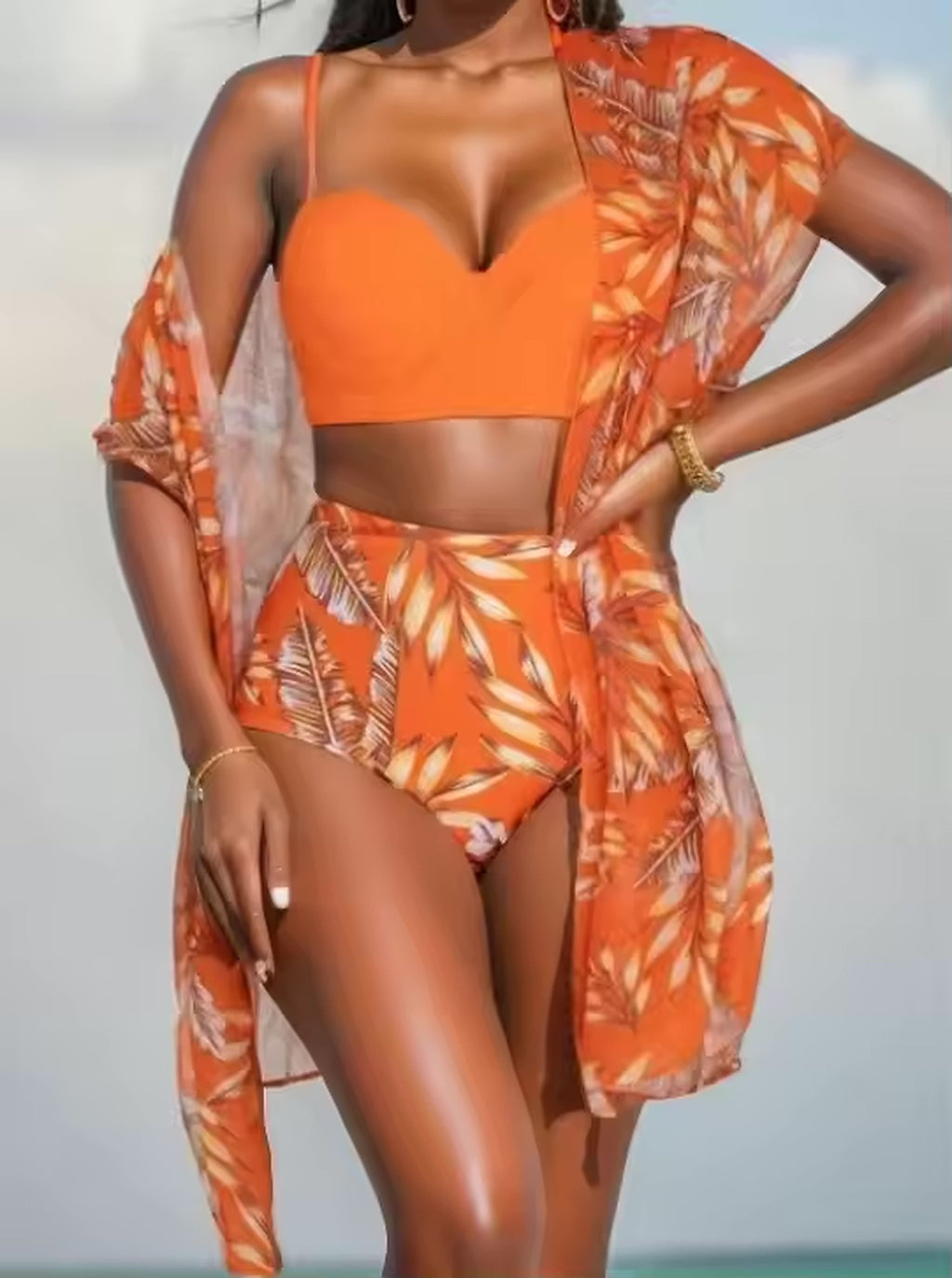 Woman wearing orange sweetheart bikini with matching tropical leaf cover-up by the sea